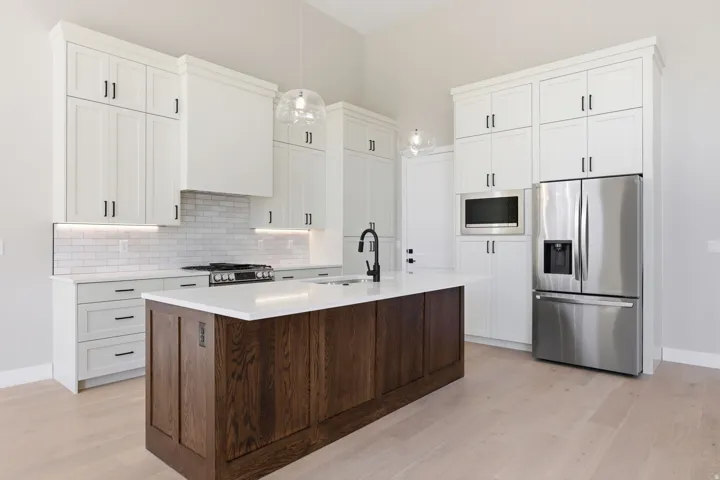 Two tone kitchen with stainless steel appliances, dual tone cabinets, light wood-style flooring, a kitchen island with sink, and decorative light fixtures