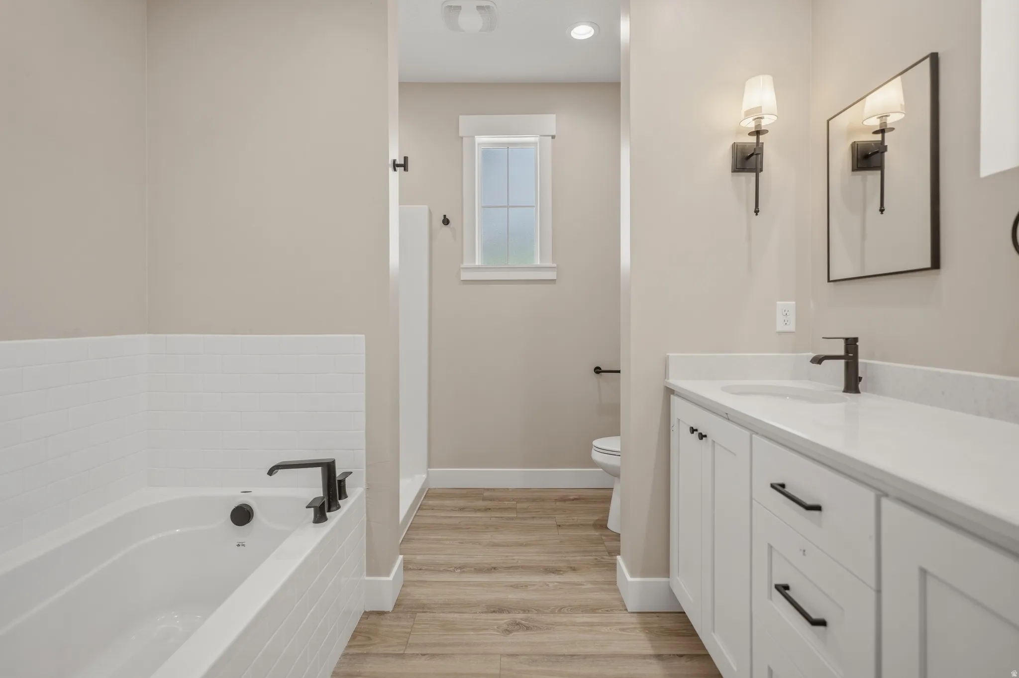 Bathroom featuring vanity, a garden tub, light wood-style floors, and recessed lighting