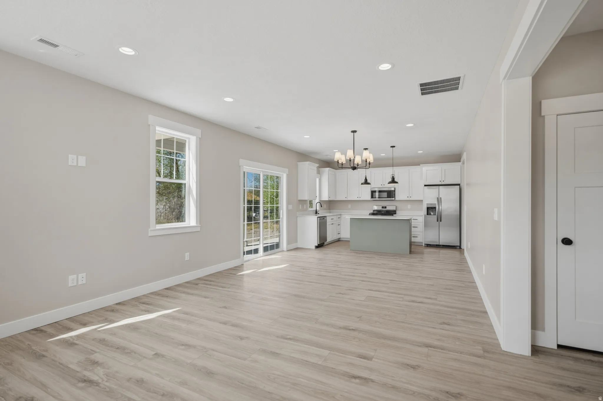 Two tone kitchen featuring open floor plan, suspended lighting, light countertops, stainless steel appliances, and two tone cabinetry