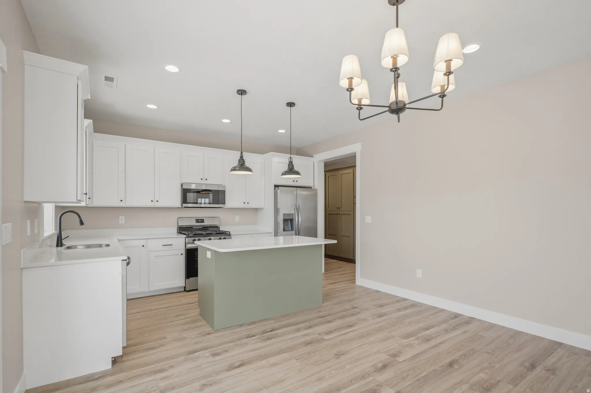 Two tone kitchen featuring stainless steel appliances, a center island, light wood-type flooring, a chandelier, and dual tone cabinets