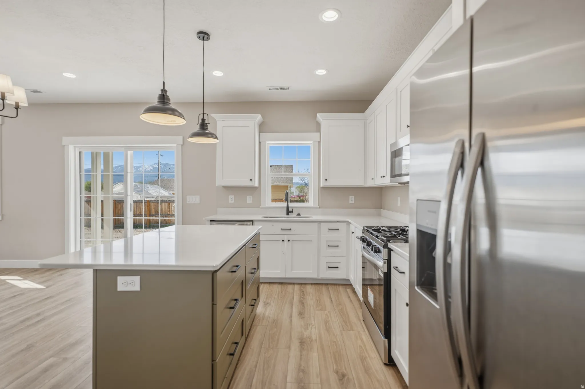 Kitchen with stainless steel appliances, dual tone cabinetry, light wood-style flooring, a kitchen island, and pendant lighting