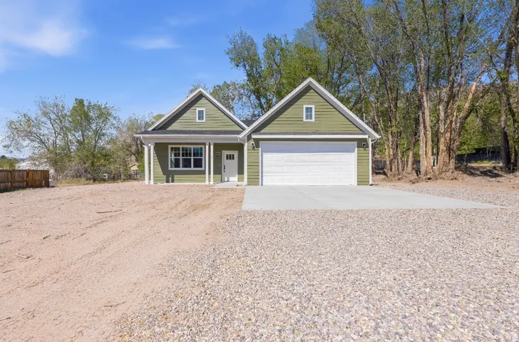 Green siding exterior with white trim, covered front porch, attached garage with white door, and concrete driveway