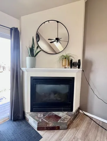 Detailed view of a glass covered fireplace, wood finished floors, and a ceiling fan