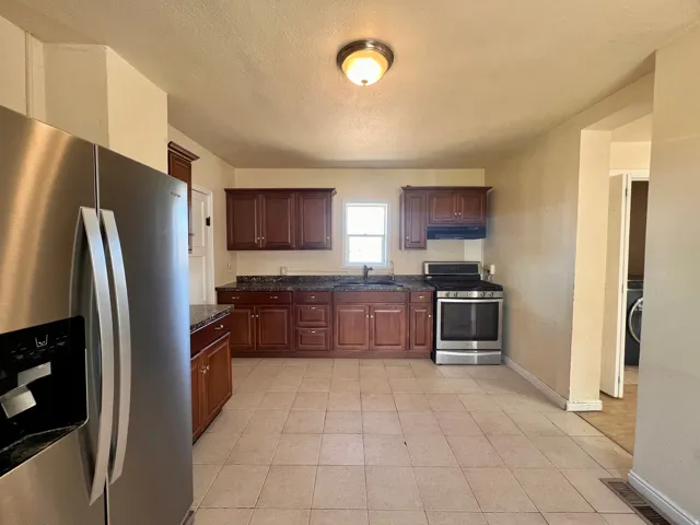 Kitchen featuring stainless steel appliances, wood cabinetry, stone-finish countertops, tile flooring, and ceiling-mounted light fixture