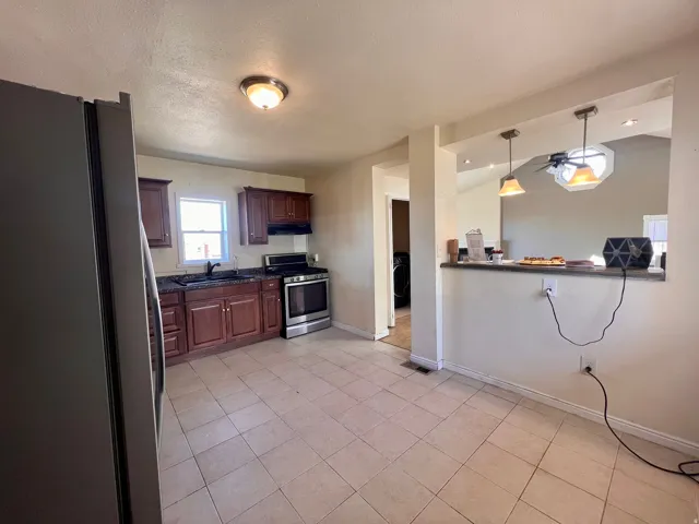 Kitchen with tiled flooring, rich wood-finish cabinetry, dark countertops, and stainless steel appliances