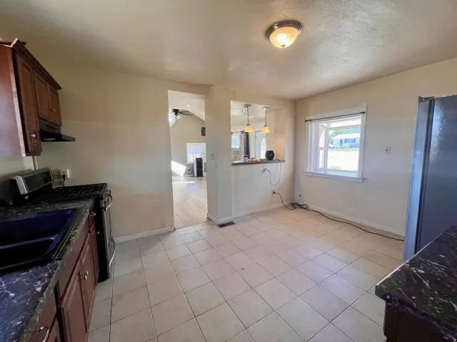 Kitchen featuring tile flooring, dark wood-finish cabinetry, dark speckled countertops, and a stainless-steel range with an overhead vent