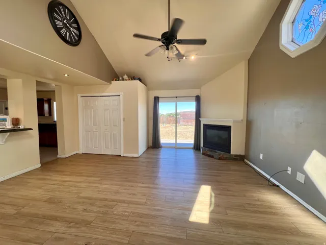 Vaulted ceilings with a ceiling fan, wood-finish flooring, a fireplace with a stone hearth, and sliding glass doors