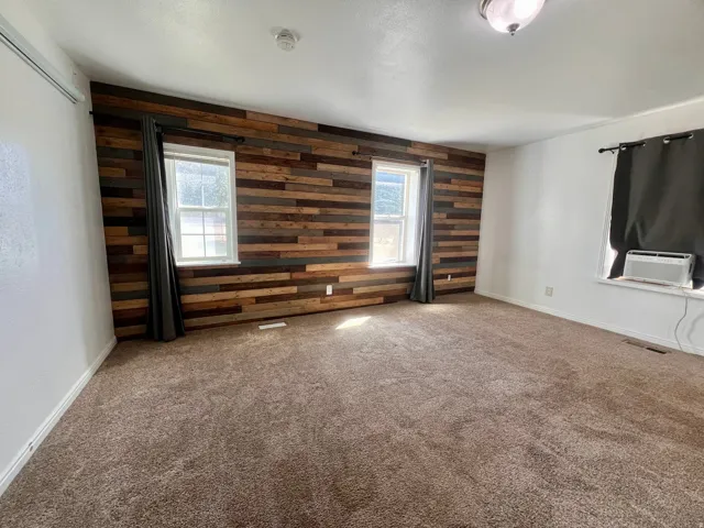 Textured wood-panel accent wall, neutral carpet flooring, multiple windows, and white painted walls