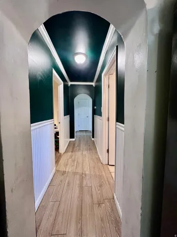 Hall featuring arched walkways, wainscoting, light wood finished floors, and ornamental molding