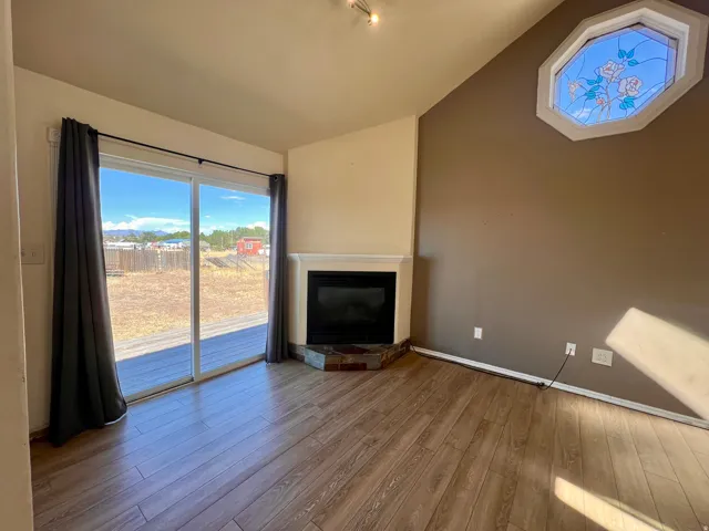 Vaulted ceiling, wood-finish flooring, corner fireplace with stone surround, stained glass octagonal window, and sliding glass door