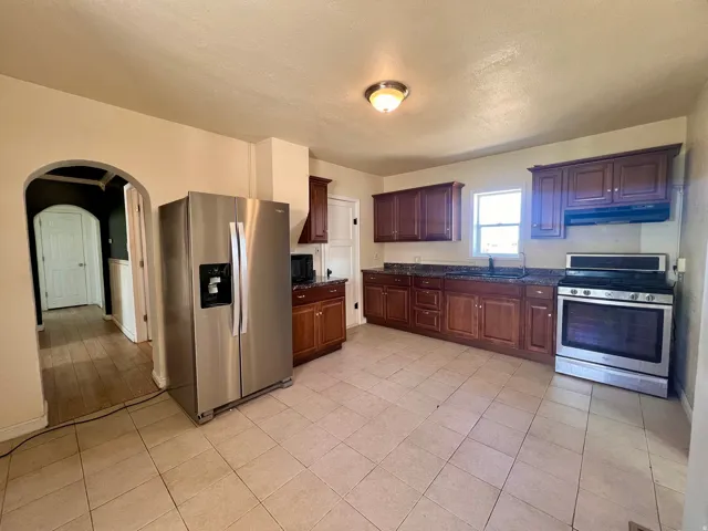 Kitchen featuring tile flooring, wood cabinetry, dark countertops, a stainless steel refrigerator, and a stainless steel range