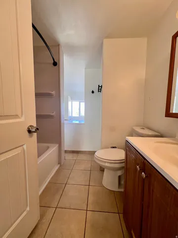 Tiled flooring, wood-finish vanity with an integrated sink, and a toilet