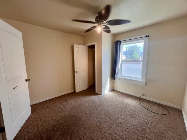 Carpeted room featuring a ceiling fan with integrated lighting, a window with a curtain rod, and a built-in closet with a panel door