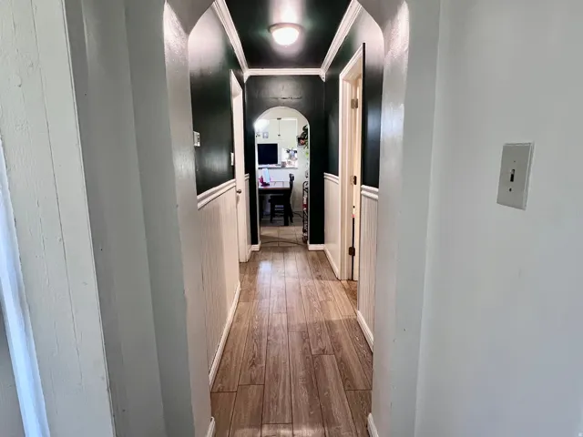 Hall with wood-type flooring, arched walkways, ornamental molding, and a wainscoted wall