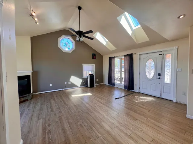 Vaulted ceiling with skylights, wood-finish flooring, white fireplace, decorative octagonal window, and a white front door with decorative glass