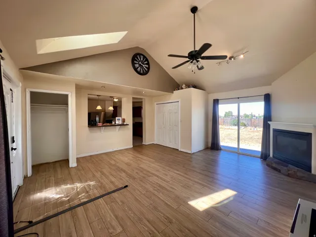 Vaulted ceiling with skylight, wood-finish flooring, built-in fireplace with stone hearth, sliding glass door, and a pass-through opening to an adjacent space