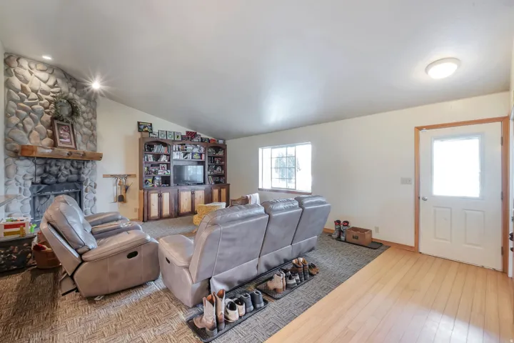 Living area featuring vaulted ceiling, light wood-type flooring, and a stone fireplace