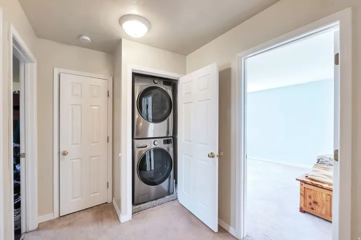 Laundry area with light colored carpet and stacked washer / dryer