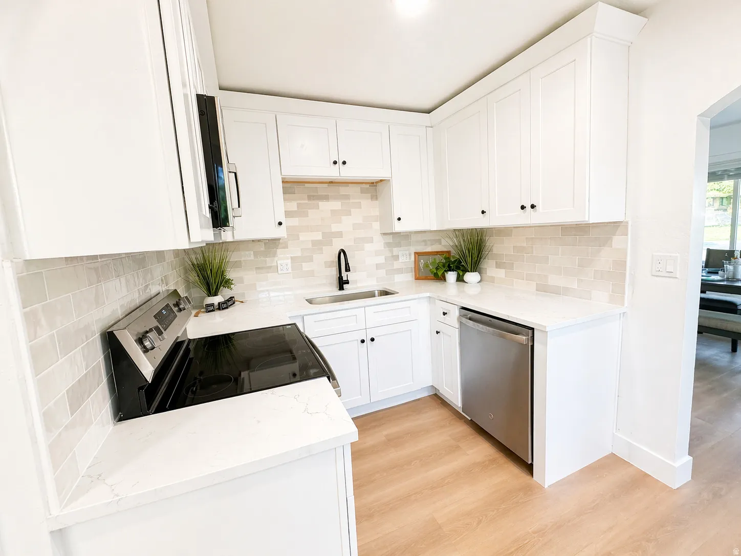 Kitchen with light stone countertops, stainless steel appliances, light wood-style flooring, white cabinets, and tasteful backsplash