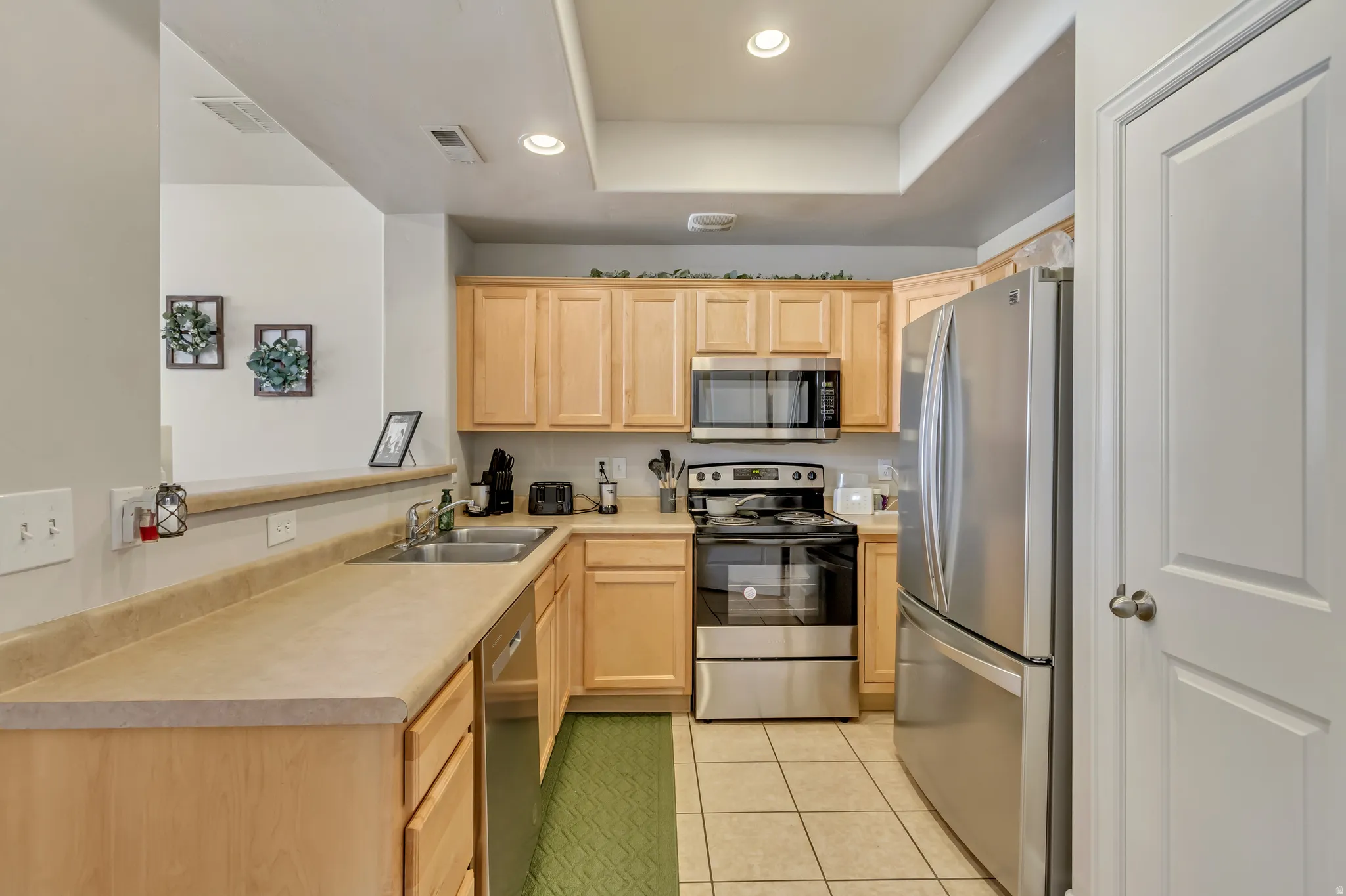 Kitchen featuring light wood finish cabinetry, stainless steel appliances, light countertops, recessed lighting, and a tray ceiling