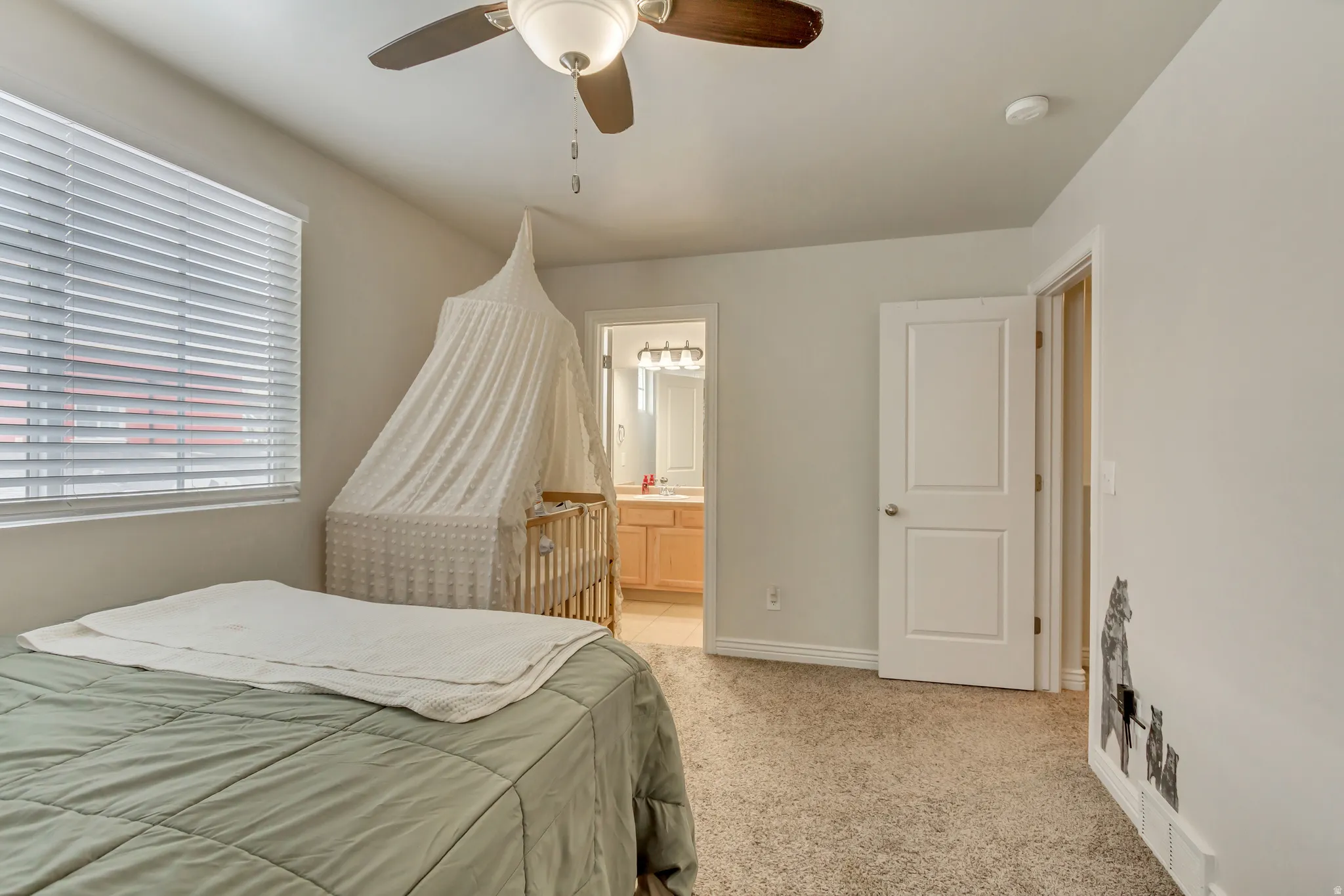 Bedroom with ensuite bathroom, light colored carpet, and a ceiling fan
