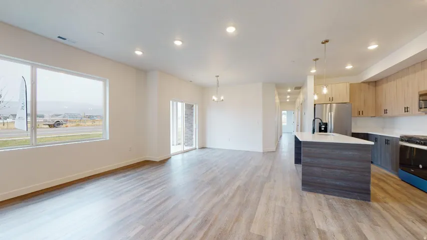 Two tone kitchen with modern cabinets, stainless steel appliances, pendant lighting, open floor plan, and light wood-type flooring