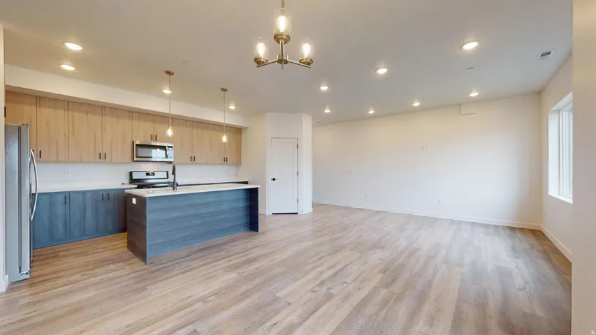 Kitchen with open floor plan, a center island with sink, stainless steel appliances, modern cabinets, and light wood finished floors