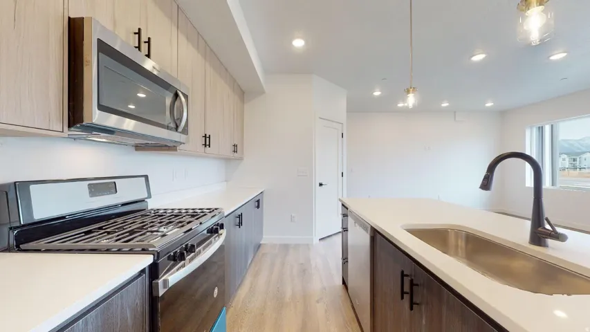 Kitchen featuring stainless steel appliances, light wood-style floors, decorative light fixtures, dual tone cabinets, and light stone counters