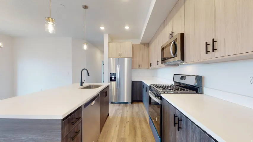 Kitchen with stainless steel appliances, light wood-type flooring, a center island with sink, modern cabinets, and hanging light fixtures