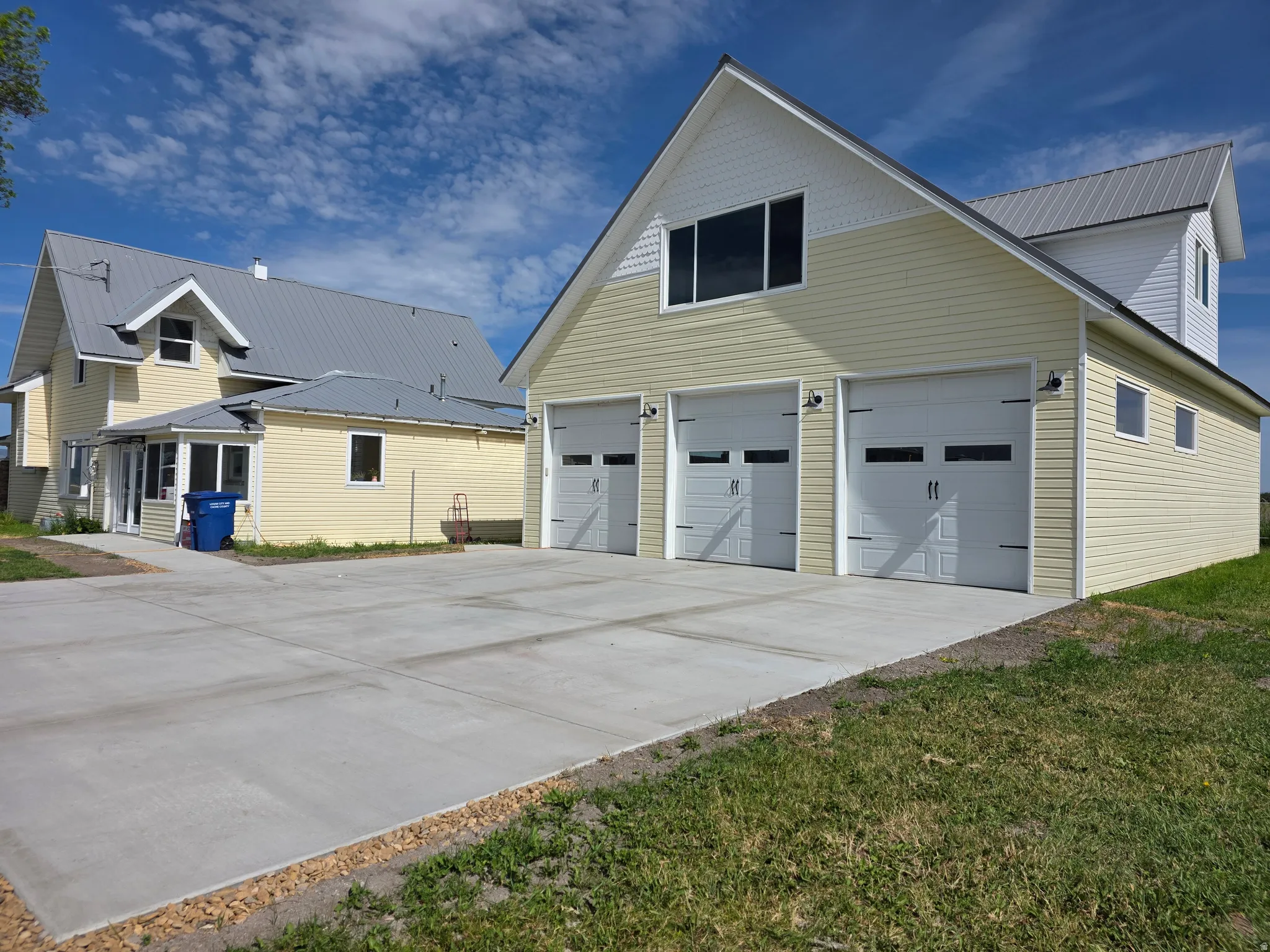 Detached multi-car garage with three overhead doors, yellow siding, and a metal roof