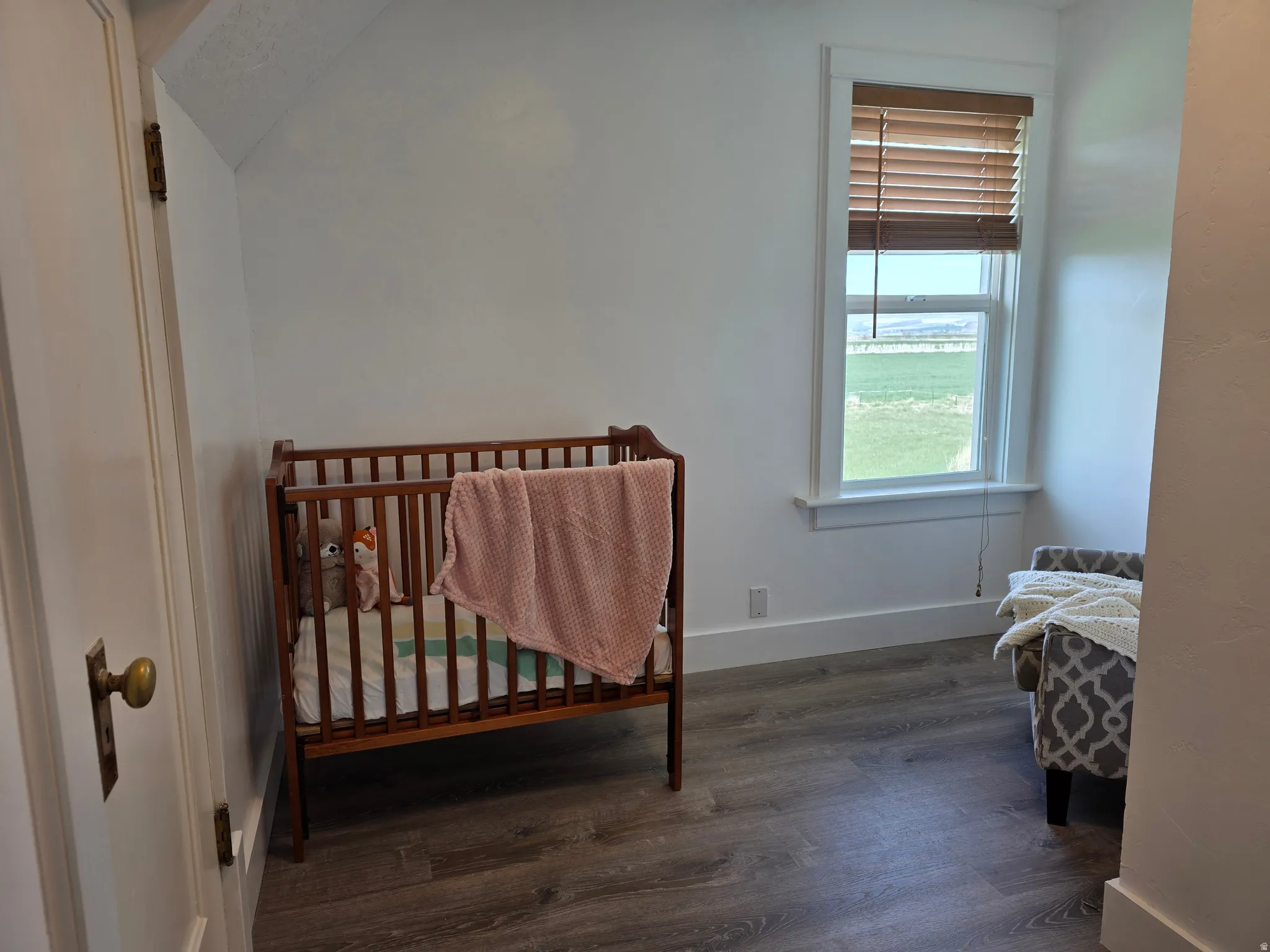Bedroom with a crib, dark wood-style flooring, and lofted ceiling