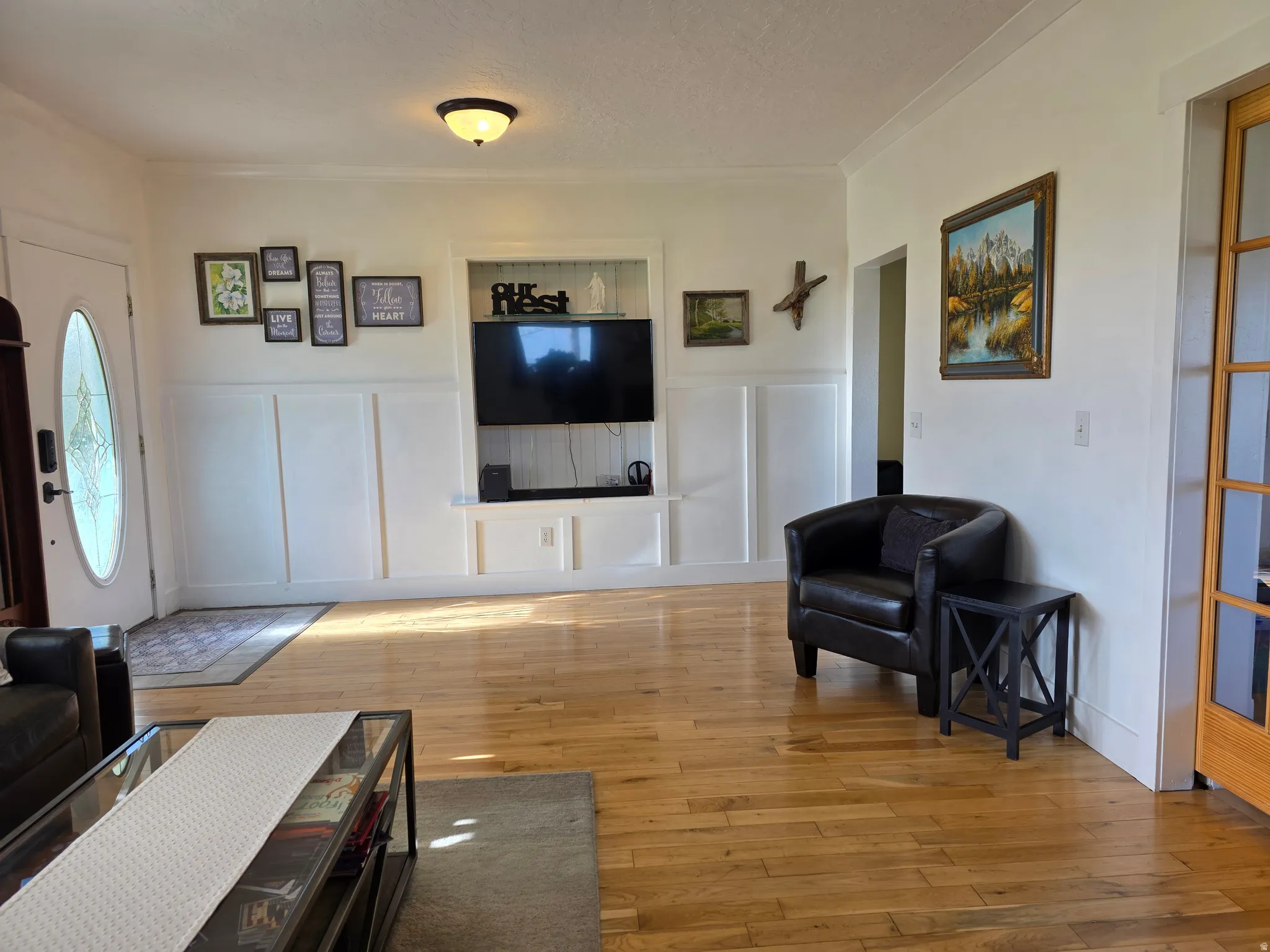 Living area featuring a decorative wall, light wood finished floors, a wainscoted wall, and ornamental molding