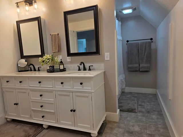 Full bathroom featuring double vanity, vaulted ceiling, and a shower with shower curtain