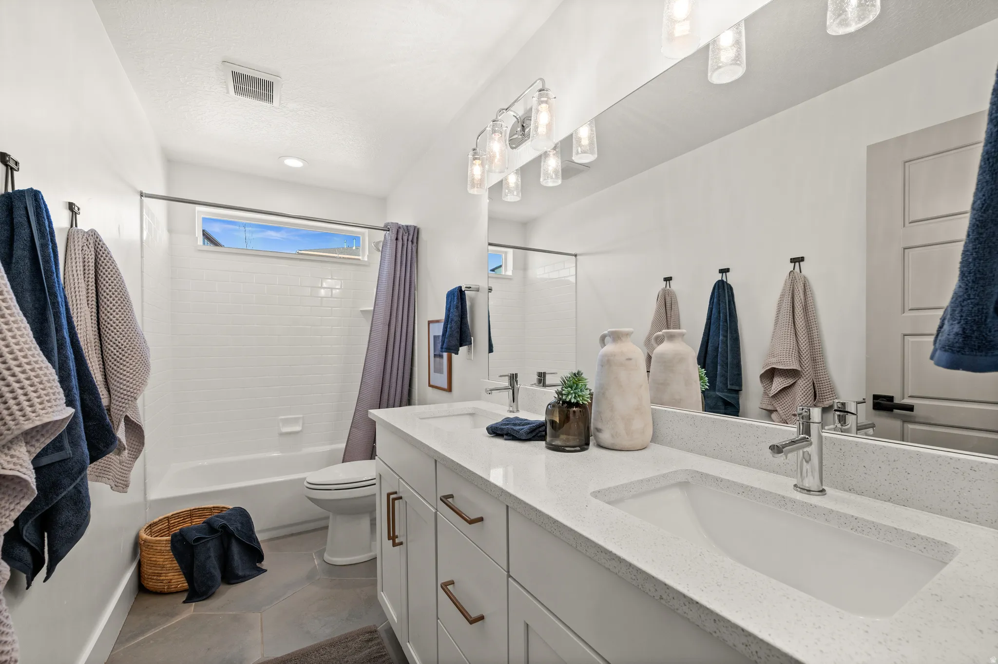 Full bathroom with double vanity, shower / bath combo, and light tile patterned floors