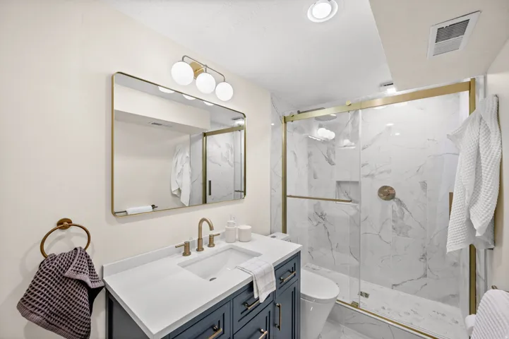 Bathroom featuring vanity, a marble finish shower, and light marble finish flooring