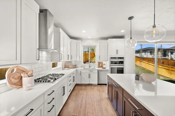 Dual tone kitchen featuring dual tone cabinets, stainless steel appliances, light wood-style flooring, backsplash, and pendant lighting