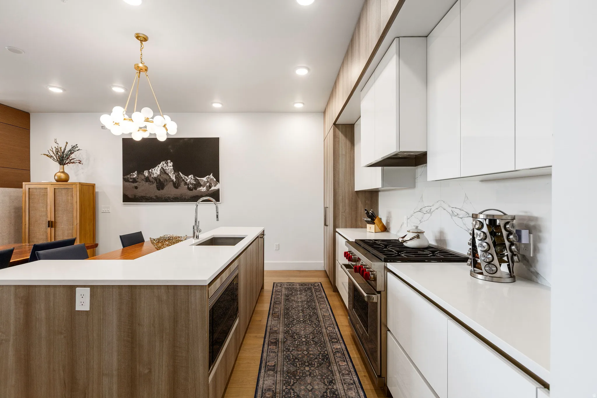 Two tone kitchen with modern cabinets, stainless steel appliances, two tone color scheme, light wood-style flooring, and suspended lighting