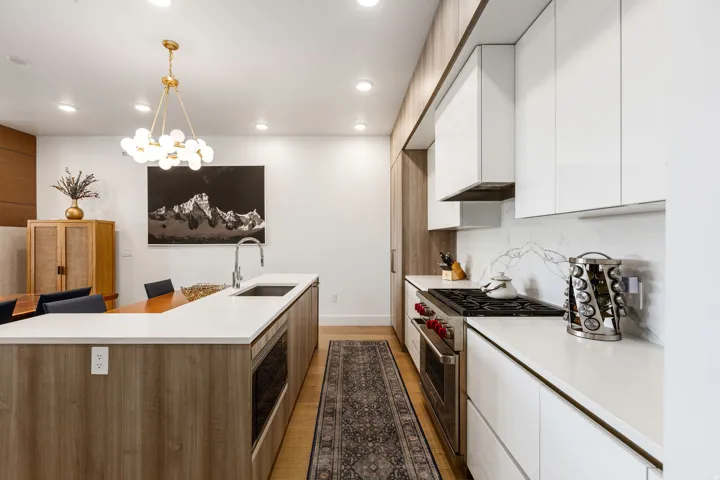 Two tone kitchen with modern cabinets, stainless steel appliances, two tone color scheme, light wood-style flooring, and suspended lighting