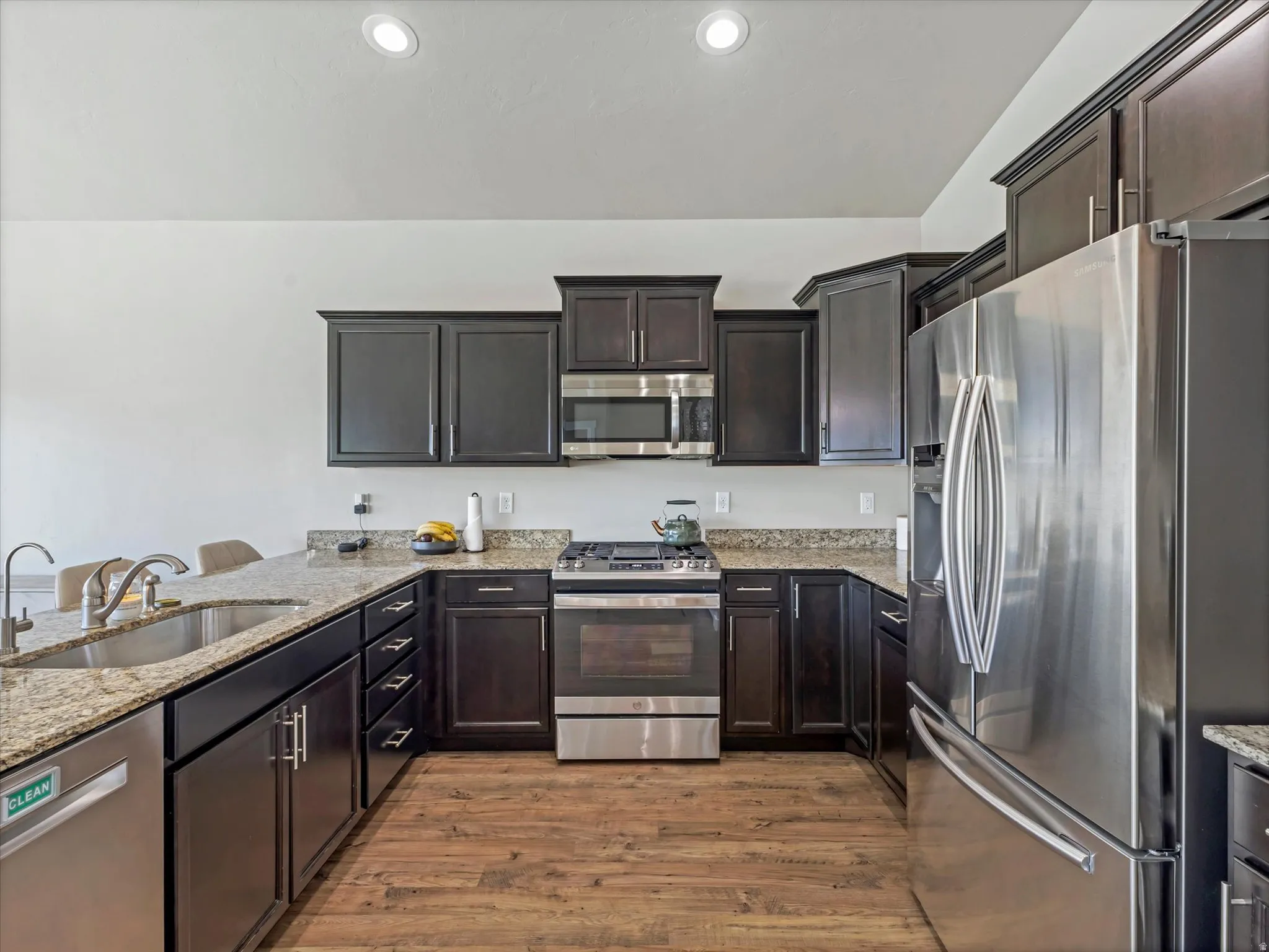 Kitchen with stainless steel appliances, light stone counters, dark wood finish cabinets, light wood finished floors, and recessed lighting