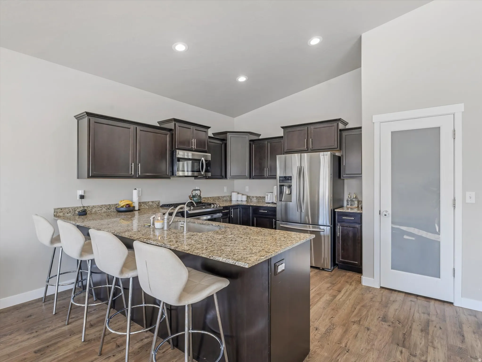 Kitchen featuring dark wood finish cabinets, a peninsula, a kitchen breakfast bar, light stone countertops, and stainless steel appliances
