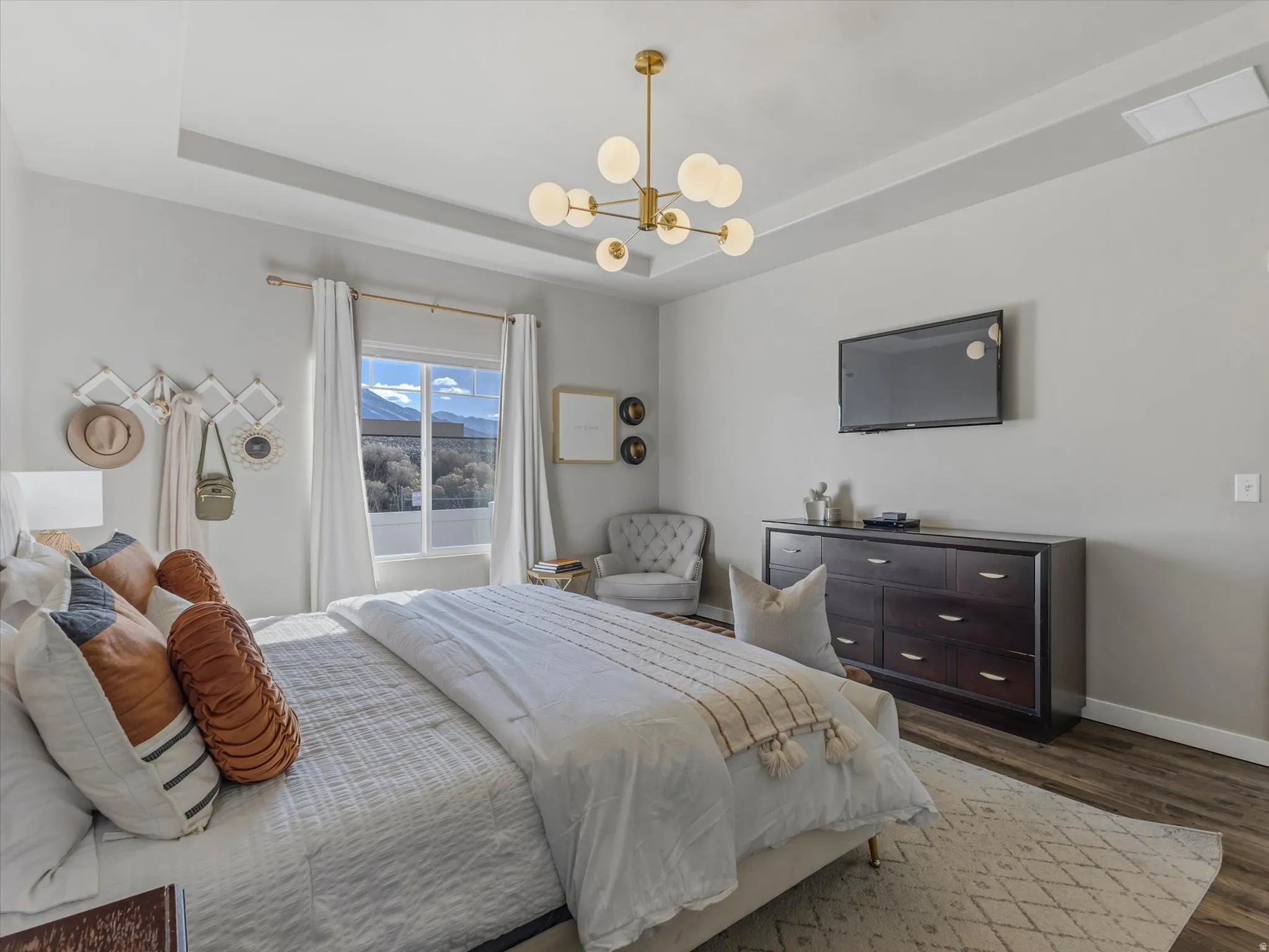 Bedroom with suspended lighting, a tray ceiling, and wood finished floors
