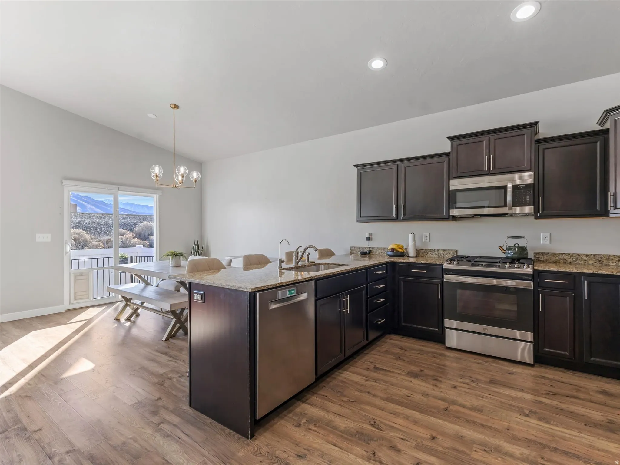 Kitchen with a peninsula, stainless steel appliances, dark wood finish cabinets, light stone countertops, and vaulted ceiling