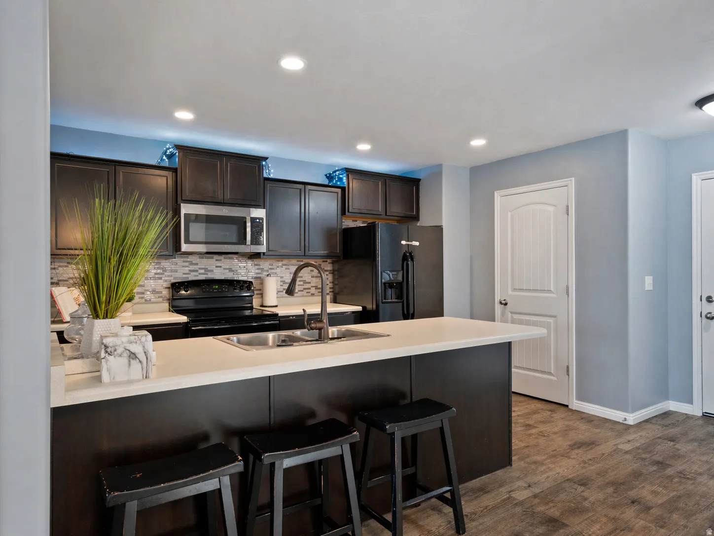 Kitchen featuring a breakfast bar, dark wood finish cabinets, a peninsula, black appliances, and backsplash