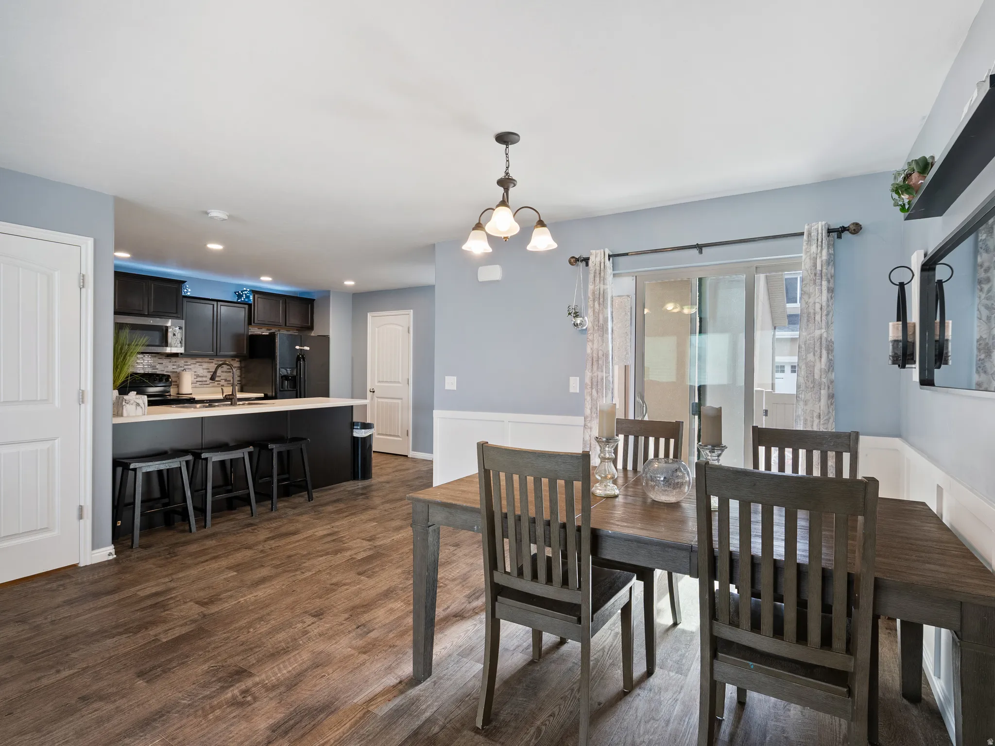 Dining room featuring dark wood-style floors, suspended lighting, and a wainscoted wall