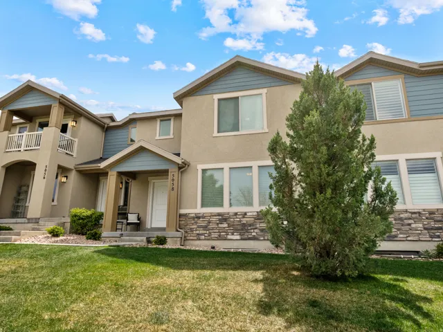 View of front of home featuring a front lawn, stucco siding, stone siding, and a balcony