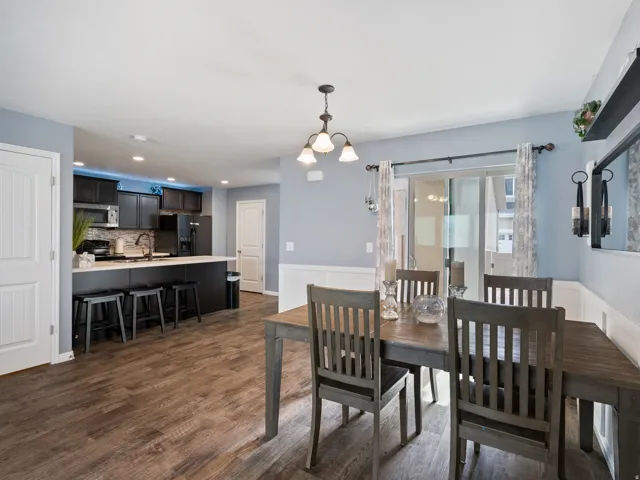 Dining room featuring dark wood-style floors, suspended lighting, and a wainscoted wall