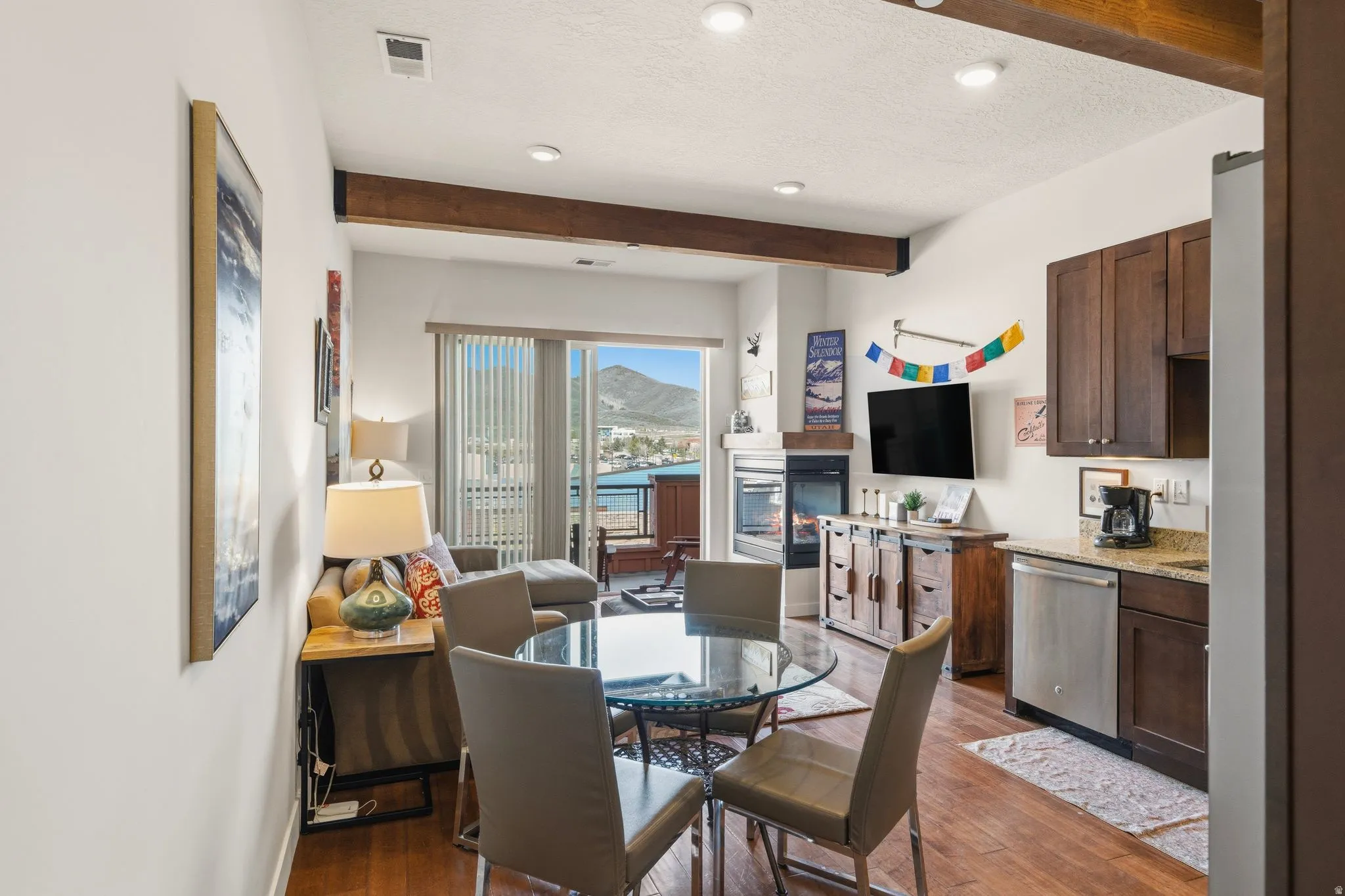 Dining space featuring a textured ceiling, a glass covered fireplace, beamed ceiling, dark wood-style floors, and recessed lighting