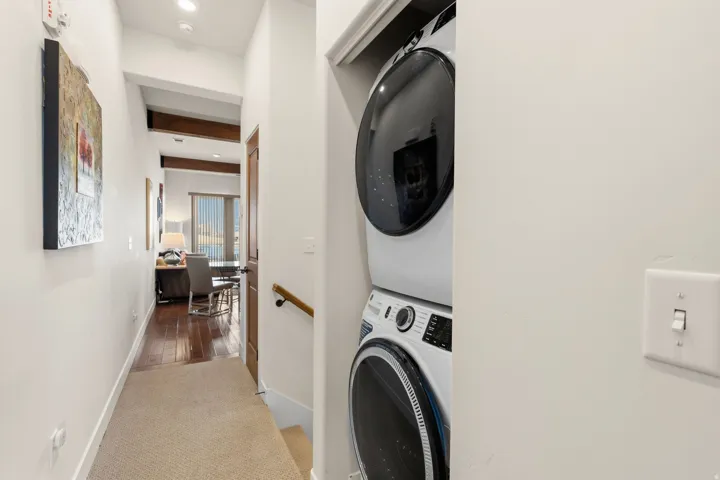 Laundry area with light carpet, stacked washer and dryer, recessed lighting, and beamed ceiling
