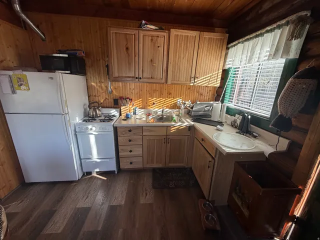 Kitchen with white appliances, light countertops, dark wood-style floors, wood walls, and wood finish cabinets