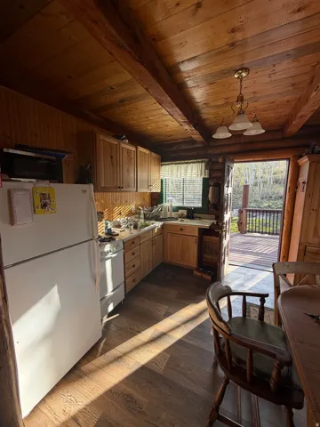 Kitchen featuring white appliances, dark wood-style floors, light countertops, decorative light fixtures, and log walls